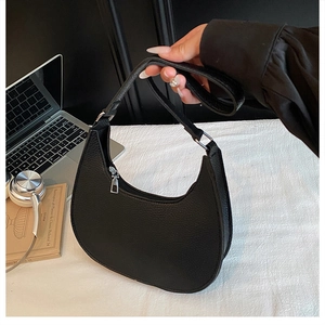 Detail of black pebbled leather half-moon bag with wide strap on a minimalist desk