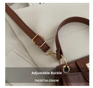 Detail of gold metal buckle and textured litchi leather shoulder strap on a brown bag