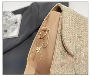 Close-up of golden alloy hardware and floral embroidery on a straw crossbody bag