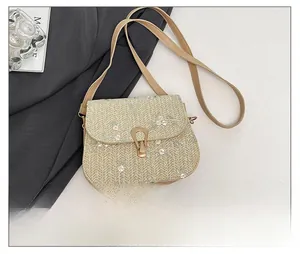 Detail showing straw saddle bag with floral embroidery and gold clasp next to a phone