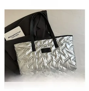 Close-up of metallic silver quilted tote bag with black handles and puffer texture