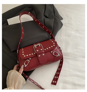 Détail d'un sac à bandoulière en cuir mat bordeaux avec rivets punk et boucle métal