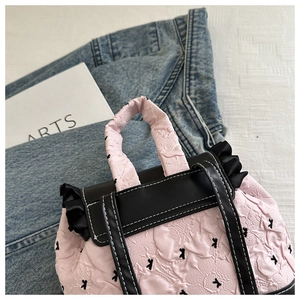Détail d'un sac à dos rose avec matelassage floral, volants noirs et sangles en cuir