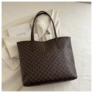 Detail of large brown tote bag with M-letter pattern and dual leather shoulder straps