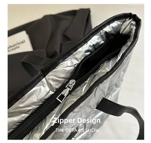 Detail of a silver quilted tote bag showing the top black zipper closure and metallic finish