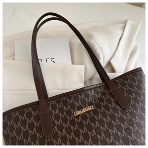 Close-up of brown tote bag with letter print pattern and golden logo plate detail