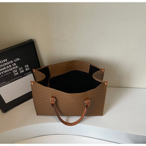 Detail view of large brown tote bag with M-pattern print and orange leather handles