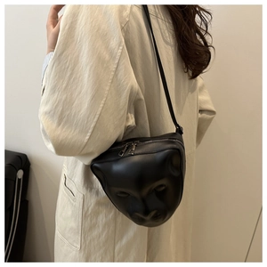 Détail du visage en relief 3D sur sac bandoulière noir avec finition cuir mat et zips