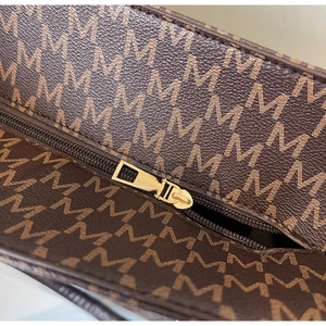 Detailed close-up of dark brown tote bag featuring golden zipper and 'M' pattern print