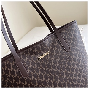 Close-up of the tote bag showing the gold metal brand plate and letter M monogram pattern