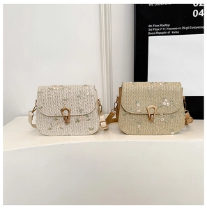 Close-up of floral embroidery and metal buckle on straw saddle bags in two colors