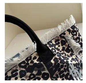 Detail of leopard print tote bag featuring white fringe edges and black ribbon handles