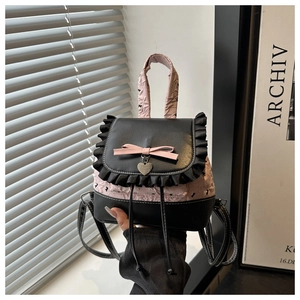 Détail de nœud rose, pendentif cœur et dentelle sur un sac à dos en cuir noir et rose