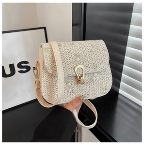 Detailed close-up of woven cream bag with floral embroidery and gold metal clasp lock
