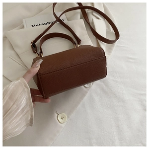 Close-up of brown litchi pattern leather cylinder bag with gold hardware and top handle