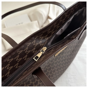 Close-up of golden metal zipper and monogram pattern on brown commuter tote bag