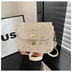 Close-up of floral embroidery on straw crossbody bag with gold metal buckle
