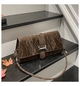Detail of dark coffee baguette bag with pleated texture and silver metal buckle