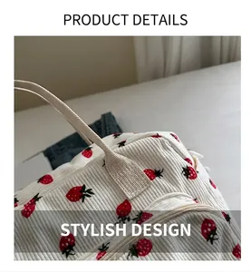 Close-up of white corduroy handbag featuring red strawberry print and gold zipper detail