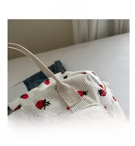 Close-up of white corduroy handbag featuring red strawberry print and gold zipper detail