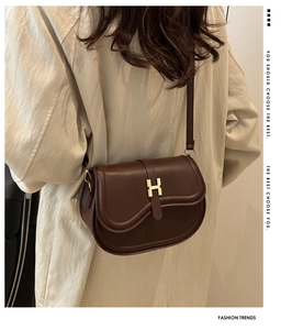 Detail view of brown semi-circular saddle bag with golden H clasp on a model shoulder