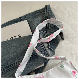 Detail of floral printed canvas shoulder bag showing white zipper and rose pattern texture
