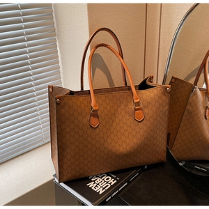 Macro view of brown monogram tote bag with leather handles and side metal buckle details