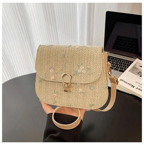 Close-up of woven straw handbag with floral embroidery and golden metal lock detail