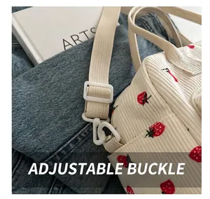 Detail of strawberry print corduroy bag showing the adjustable beige woven strap buckle
