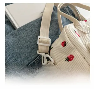 Detail of strawberry print corduroy bag showing the adjustable beige woven strap buckle
