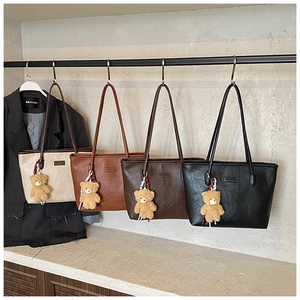 Four colors of minimalist leather tote bags with cute teddy bear charms on a display rack