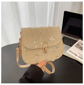 Detail of beige straw crossbody bag with floral embroidery and gold horseshoe lock