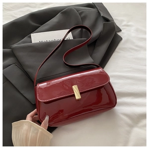 Detail of burgundy patent leather shoulder bag with a gold buckle on a grey blazer