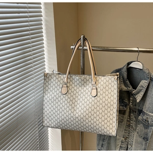 Detail of a minimalist cream tote bag with black letter print and leather handles