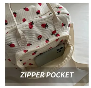 Detail of white corduroy lunch bag with red strawberry print showing the front zipper pocket
