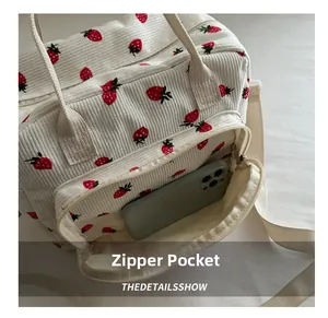 Detail of white corduroy lunch bag with red strawberry print showing the front zipper pocket