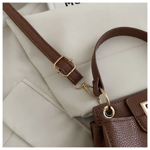Detail of brown litchi pattern leather bag showing golden metal buckle and hardware hooks