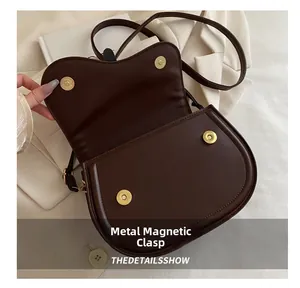 Detail view of the golden magnetic closure on a dark brown saddle bag with matte finish