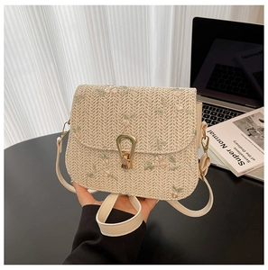 Detail of floral embroidery on a beige straw bag with a metal buckle and shoulder strap