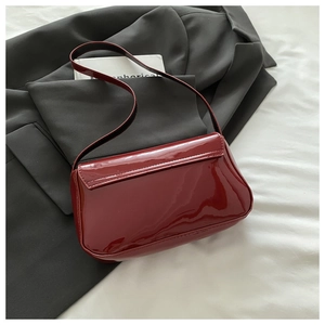Close-up of a glossy deep red patent leather shoulder bag on a black blazer