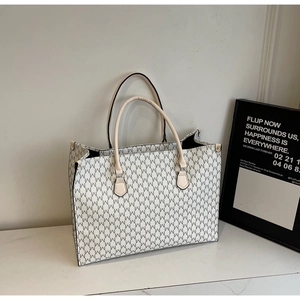 Close-up of spacious tote bag featuring repetitive M-letter prints and beige slim handles