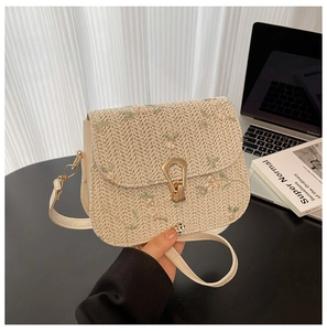 Detail of floral embroidery and golden horseshoe clasp on beige straw crossbody bag