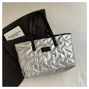 Detail of silver metallic quilted tote bag with black shoulder straps and brand label