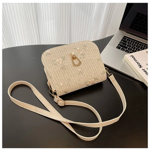 Detailed view of floral embroidery on a straw crossbody bag with golden metal clasp