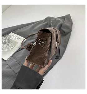 Detail of a brown pleated leather shoulder bag with a silver buckle and knotted strap