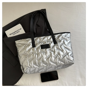 Close-up of silver quilted tote bag featuring metallic finish and black leather strap