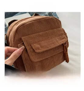 Detailed close-up of brown corduroy crossbody bag with woven zipper pull and front pocket