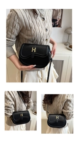 Detail of a black leather crescent saddle bag featuring a gold H buckle and strap