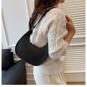 Close-up of black lychee texture crescent bag worn by a model in a minimalist modern setting