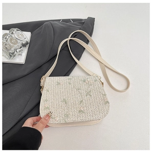 Detail of hand-woven straw bag featuring delicate floral embroidery and gold metal clasp